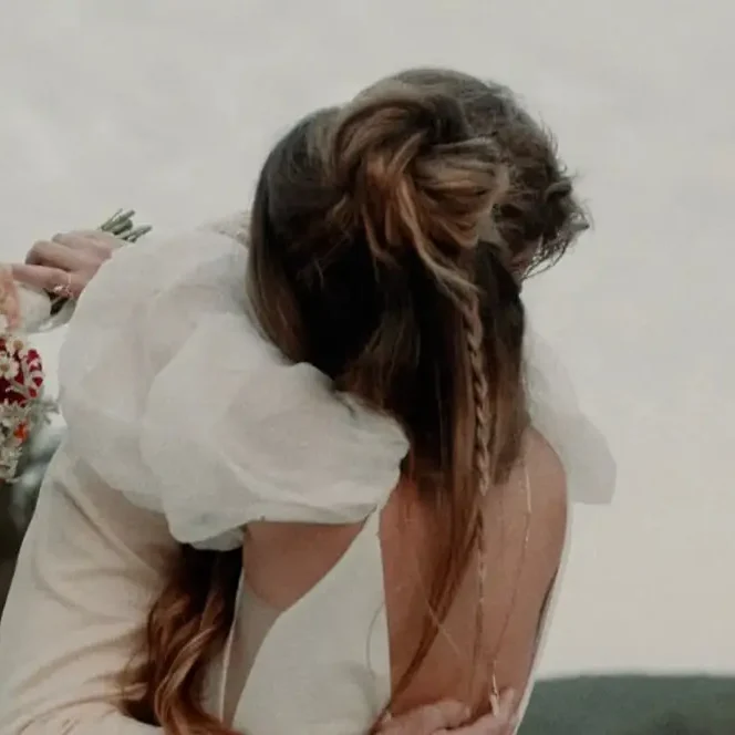 Une mariée aux cheveux tressés enlace son partenaire en tenant un bouquet coloré de fleurs d’été.