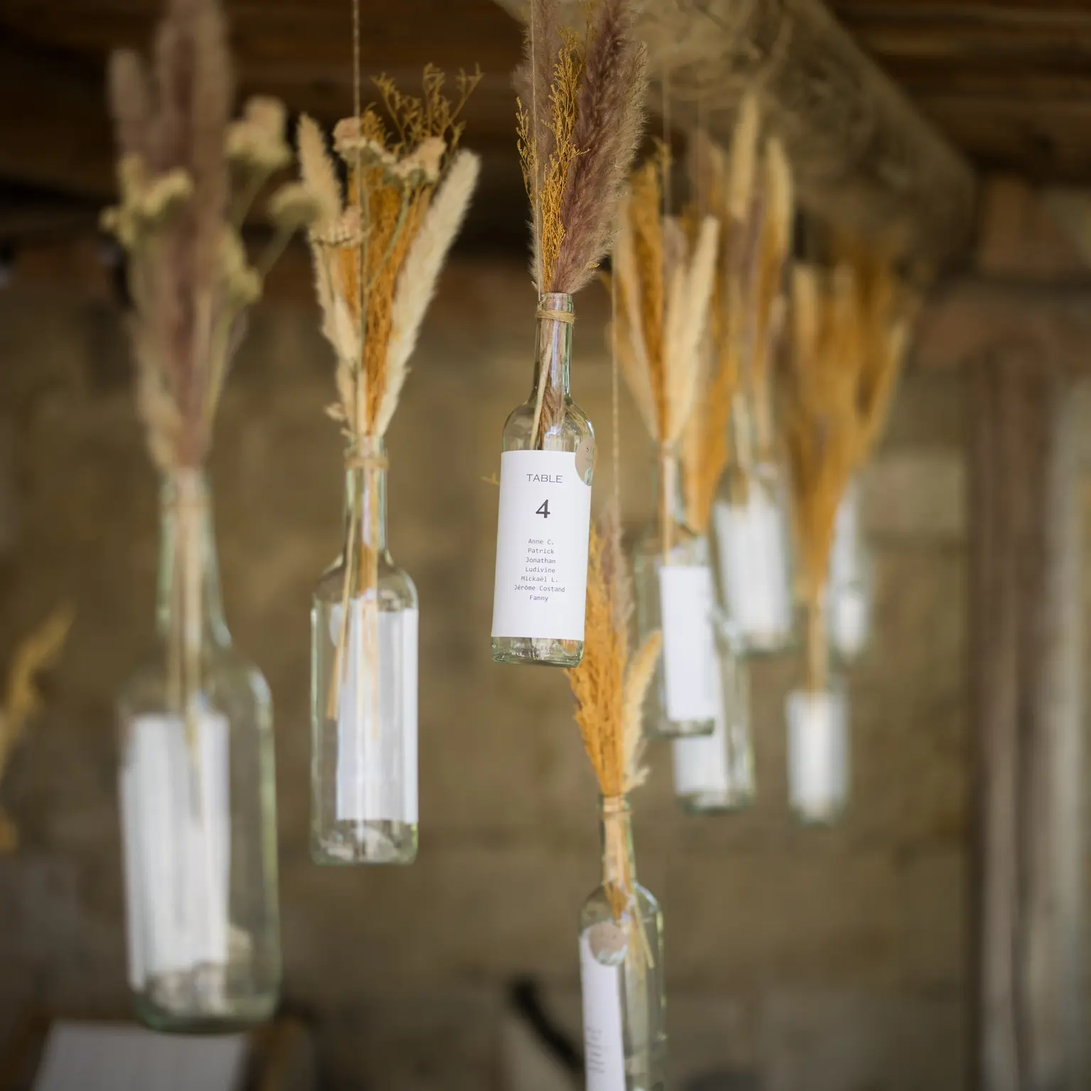 Décoration de mariage YelloEvent, bouteilles suspendues servant de plan de table avec fleurs séchées pour une ambiance champêtre et raffinée