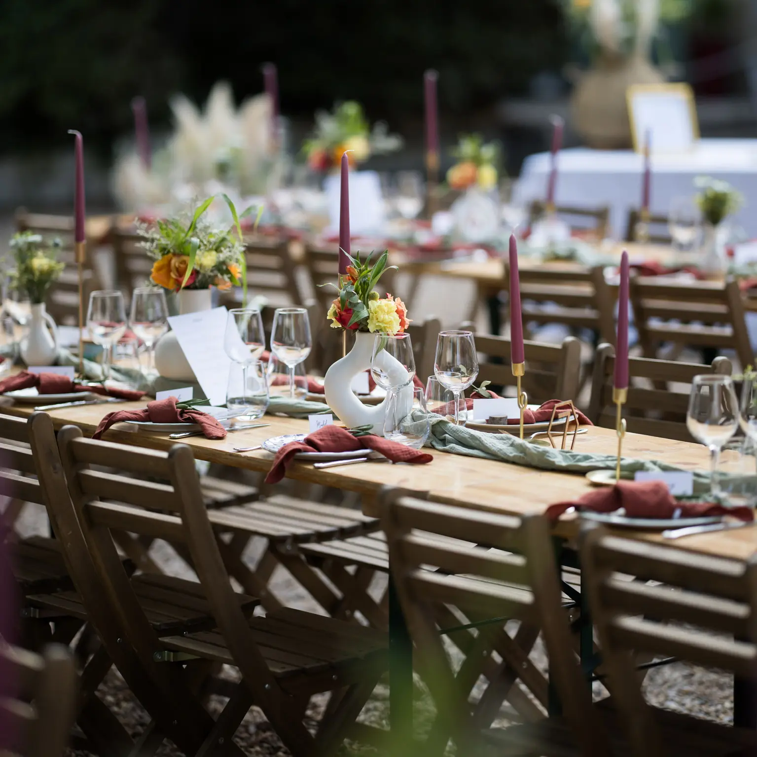 Grande table de mariage dressée en extérieur, ornée de bougies mauves, de fleurs colorées et de vases design, créant une ambiance raffinée et conviviale