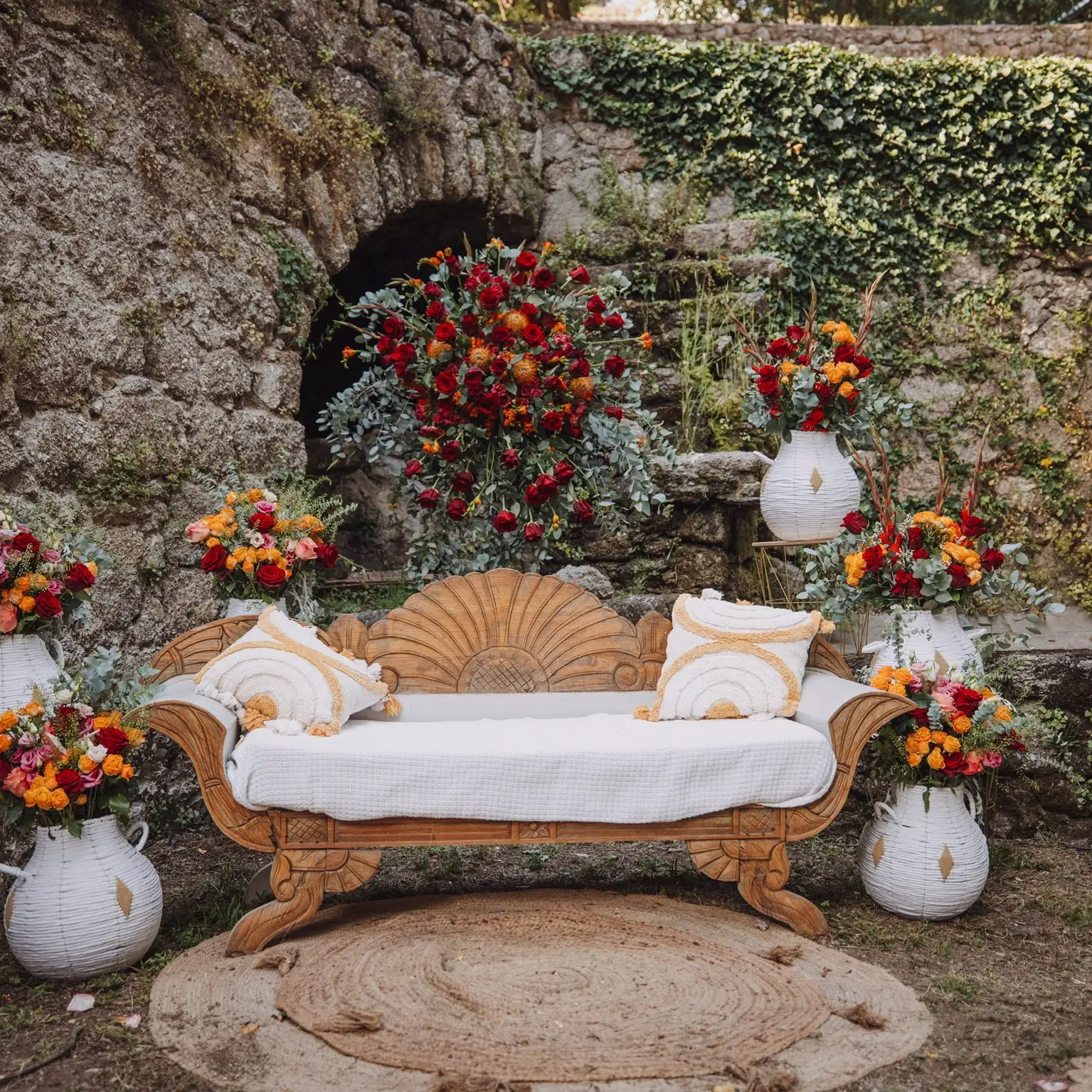 Coin détente bohème chic signé YelloEvent, canapé en bois sculpté entouré de compositions florales rouge et orange dans un jardin du Sud de la France