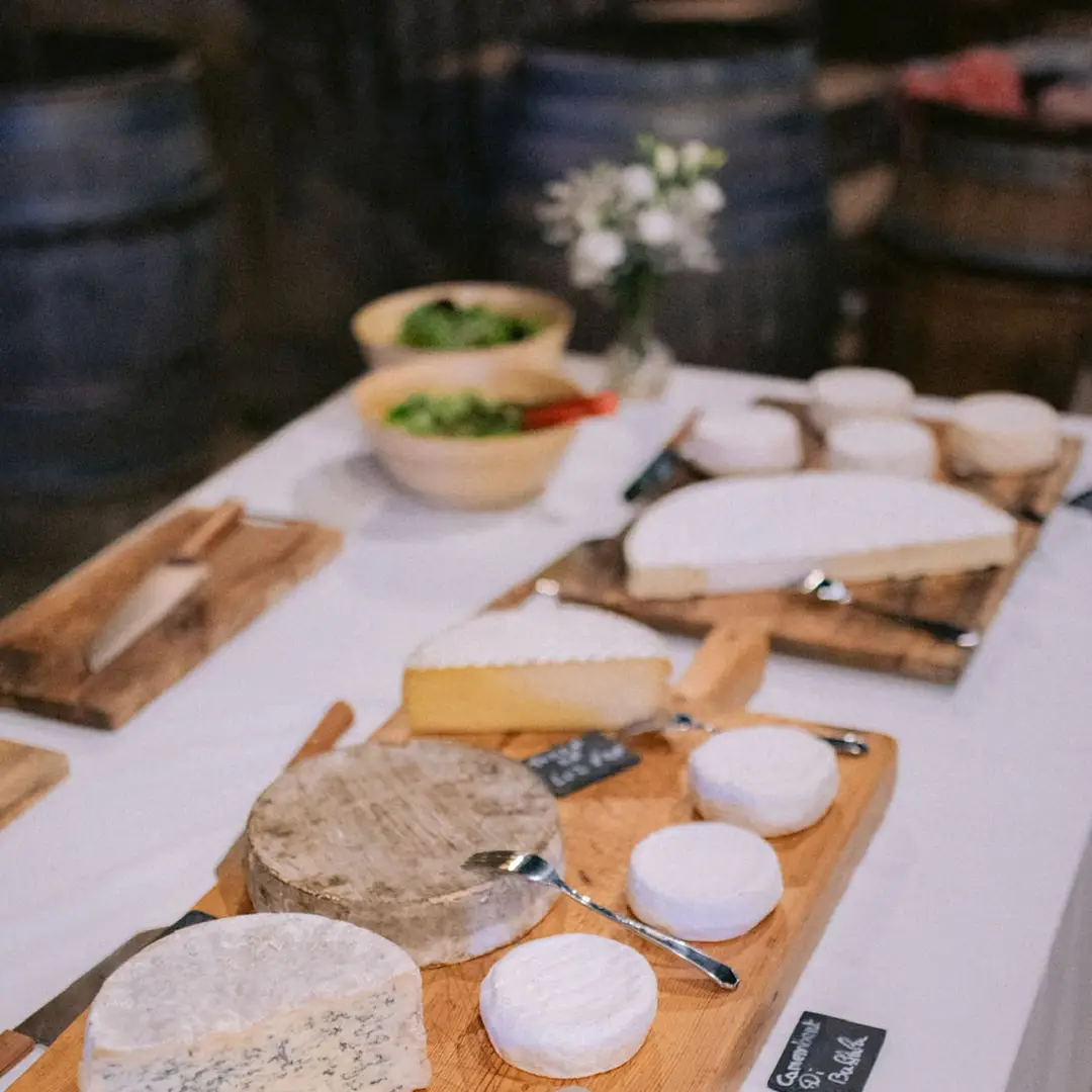 Assortiment de fromages affinés sur planches en bois avec salades en arrière-plan – buffet mariage Yello Event
