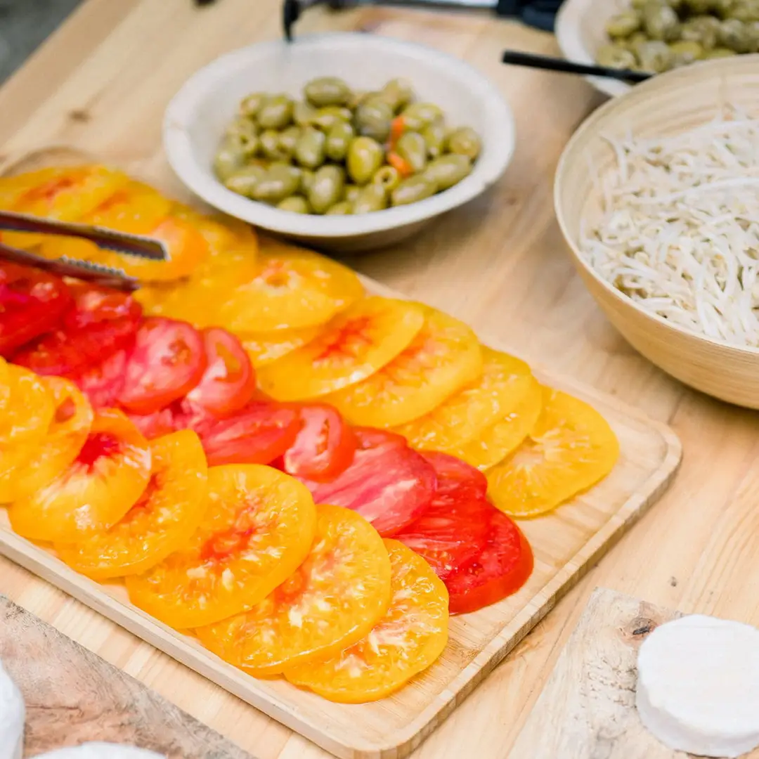 Buffet traiteur avec tranches de tomates jaunes et rouges, olives vertes et crudités – Yello Event