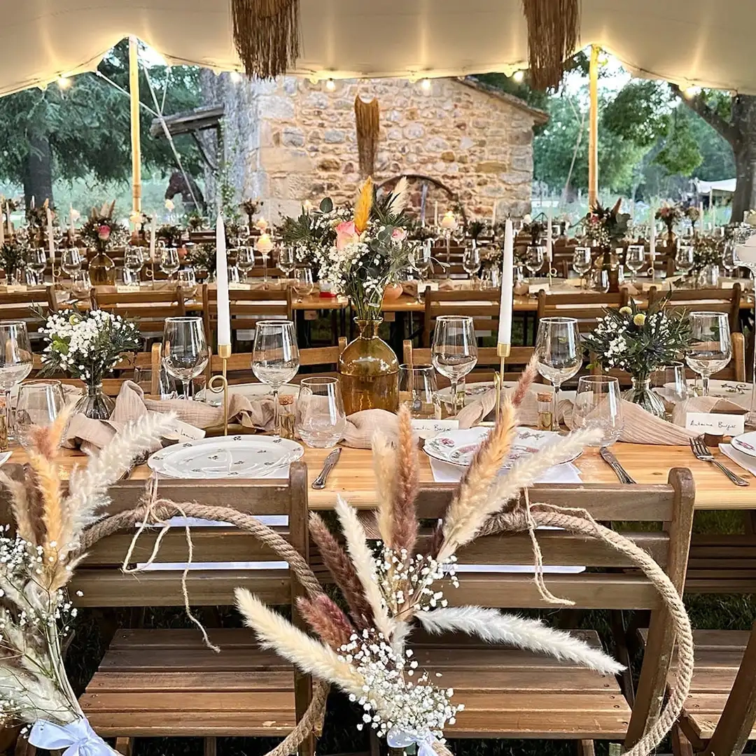 Grande tablée de mariage champêtre dressée sous une tente, décorée de fleurs séchées, de bougies et de vaisselle élégante.